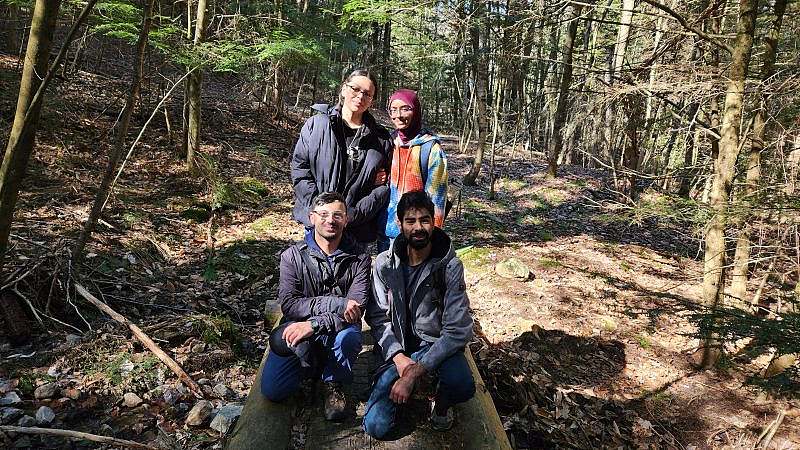 4 volunteers pose on top of bridge smiling with wooded forest in the background. 
