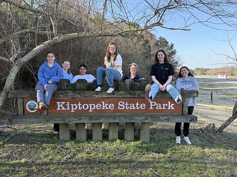Seven volunteers pose smiling by a Kiptopeke State Park Sign. 