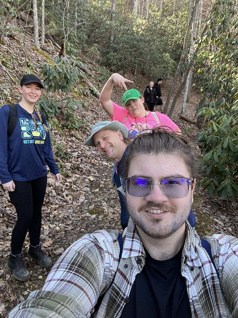 A group of 4 smiling hikers pose on a wooded trail.