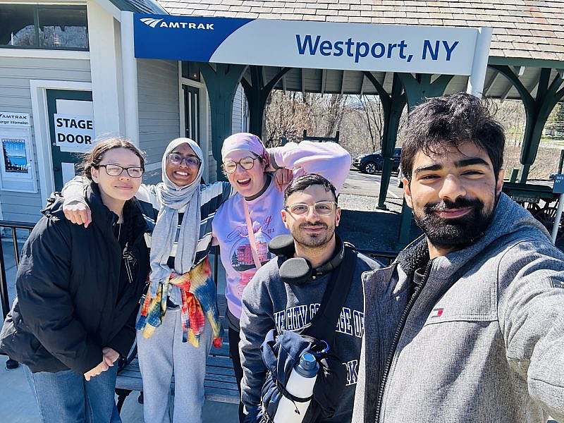 5 people take a selfie in front of an amtrack station.
